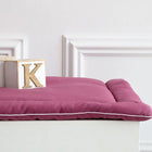 Ein Holzblock mit dem Buchstaben K ruht auf einer KraftKids Wickelauflage Leinen magenta dunkel mit weißer Paspelierung auf einem weißen Möbelstück vor einer hellen Wand mit Zierleisten.