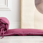 Die Bettumrandung Nestchen Leinen magenta dunkel von KraftKids mit weißer Paspel liegt auf hellem Holzboden vor abstrakter Kunst und einer weißen Wand.