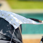 Eine Nahaufnahme des KraftKids Sonnensegel Musselin gelbe Zitronen Baldachin mit weißem Stoff und gelben Zitronen Druck, durch ein Schwimmbad mit grünem Gras-perfekt Sonnenschutz für Babys gezeigt.