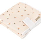 Eine gefaltete KraftKids Reisewickelunterlage Musselin Kirschen, pfirsichfarben mit Kirschenmuster und weißer Zierleiste, mit aufgenähtem Anhänger - perfekt als platzsparende Wickelunterlage für unterwegs.