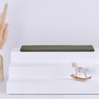 Auf einem weißen, dreistufigen Podest steht die KraftKids GmbH Sitzauflage für Ikea TROFAST Doppelkrepp in Herbstgrün. Links steht eine geflochtene Vase mit Pampasgras, rechts sitzt ein kleines weißes und hölzernes Schaukelpferd vor einem hellen Hintergrund.