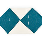 Die KraftKids Decke für Babyschale Winter Musselin besteht aus zwei petrolfarbenen Abschnitten mit goldenen Punkten und zwei weißen Abschnitten, die rautenförmig angeordnet sind. Die petrolfarbenen Abschnitte sind mit vier weißen Stoffschlaufen versehen, die auf einem weißen Hintergrund abgebildet sind.