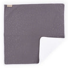 Die KraftKids Wickelunterlage Musselin goldene Punkte auf Grau ist eine quadratische graue Babydecke mit goldenen Punkten und einem weichen weißen Futter, ideal als Reisewickelunterlage oder Wickelauflage Baby. An der linken oberen Ecke ist ein hellbraunes Etikett aufgenäht.