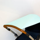 Nahaufnahme eines KraftKids-Kinderwagens mit Sonnensegel weiße Punkte auf Mint Verdeck, braunem lederbezogenem Griff und dunkelblauem Sitz vor einem schlichten weißen Hintergrund.