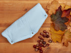 Eine blaue, handgenähte Stoffwindel mit Druckknöpfen ruht auf Holz, umgeben von Herbstblättern und Kastanien. Der weiche Fleece ist besonders kuschelig - ideal, um ihn an kühlen Tagen mit dem KraftKids Kinderwagenmuff kleine Blätter hellblau auf Weiß zu kombinieren.