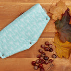 Der KraftKids Kinderwagenmuff "weiße Pfeile auf Mint" liegt auf einer Holzfläche zwischen Herbstblättern und Kastanien und hält die Hände beim Spaziergang mit dem Baby kuschelig warm.