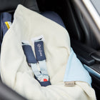 Eine KraftKids "Decke für Babyschale Winter kleine Blätter hellblau auf Weiß" bedeckt einen leeren Kindersitz auf dem Rücksitz eines Autos, wobei die cremefarbene Decke und das blau umrandete Design neben dem Sicherheitsgurt und der Innenausstattung sichtbar sind.