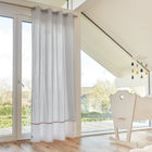 Helles, modernes Kinderzimmer mit großen Glastüren, KraftKids Gardinen Uniweiss Karo grau, hellem Holzboden, weißer Wiege und einem von der Decke hängenden Wolkenmobile. Sonnenlicht fällt ein und unterstreicht die klare, minimalistische Einrichtung.