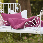 Ein weißes Metallbett mit KraftKids Bettwäscheset Musselin purpur aus 100% Baumwolle steht im Freien auf einer Wiese, umgeben von Bäumen und verziert mit weißen Sternen, und schafft einen gemütlichen, skurrilen Platz für erholsamen Schlaf.