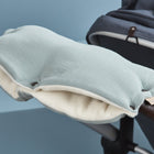 Der KraftKids Kinderwagenmuff Musselin mint ist ein weicher, gepolsterter Handwärmer in mintgrün, der von Hand genäht und für kuschelige Wärme an einem Kinderwagengriff befestigt wird. Das Produkt ist auf einem dunkelblauen Kinderwagen vor einem hellblauen Hintergrund abgebildet.