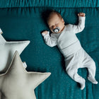 Ein Baby liegt auf einer KraftKids Krabbeldecke Musselin goldene Punkte auf Petrol mit einem sternförmigen Kissen aus weichem Polyestervlies.