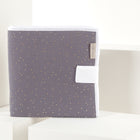 Eine Reisewickelunterlage Musselin goldene Punkte auf Grau von KraftKids ist mit kleinen goldenen Punkten und einer weißen Lasche gefaltet, aufrecht auf weißen geometrischen Blöcken vor einem neutralen Hintergrund abgebildet.