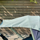 Ein KraftKids Sonnensegel Musselin goldene Punkte auf Grün ist über einen Kinderwagen mit braunem Griff drapiert, der vor einer Holzplankenwand im hellen Sonnenlicht steht.