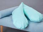 Ein Paar KraftKids qualitäts Stillkissen weiße Punkte auf Mint, V-förmig auf einer hellblauen Bank mit Holzbeinen vor einem grauen Hintergrund. Diese ergonomischen Kissen bringen Komfort und Stil in jeden Raum.
