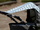 An einem grauen Kinderwagen ist der KraftKids Sonnensegel Chevron hellgrau und mint an den Griffen befestigt und bietet zusätzlichen Sitzschutz. Der Hintergrund ist im Freien und unscharf.