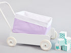 Ein weißer Spielzeugwagen mit dem KraftKids Körbchen Uniweiss weiße Punkte auf Lila sitzt neben blauen und weißen Deko-Blöcken und bietet stilvolle Aufbewahrung im Kinderzimmer vor einem hellgrauen Hintergrund.