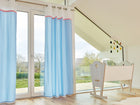 Ein helles Kinderzimmer mit großen Fenstern, hellen Holzböden und KraftKids Gardinen Uniweiss weiße Halbkreise auf Pastelblau aus 100% Baumwolle. Eine weiße Wiege steht neben einem modernen Mobile, und draußen sind Bäume und Häuser zu sehen.