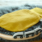 Ein KraftKids Strampelsack Frühling Sommer Doppelkrepp Gelb Senf ruht auf einem grauen Kunstfellteppich, umgeben von einer hölzernen Spielzeugeisenbahn mit einem weißen und schwarzen Zug.