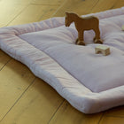 Die Krabbeldecke Doppelkrepp Rosa von KraftKids in zartem Hellrosa liegt auf einem Holzboden mit einem Holzspielzeugpferd und Bauklötzen darauf, während warmes Sonnenlicht auf die gemütliche Szene fällt.