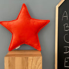 Das KraftKids Sternkissen aus Breitcord in Reinorange sitzt auf einem Holzblock neben einer Tafel mit Buchstaben - ein farbenfrohes Accessoire fürs Kinderzimmer vor grauer Wand.