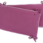 Die KraftKids Bettumrandung Nestchen Musselin purpur besteht aus zwei lilafarbenen, rechteckigen Kissen aus 100% Baumwolle mit weißem Besatz und Stoffbändern, die für zusätzlichen Komfort und Nestwärme schief gestapelt werden.