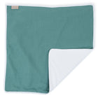 Eine quadratische nilblaue KraftKids Wickelunterlage Musselin mit weißer Unterseite, flach gelegt mit einer Ecke gefaltet, mit einem kleinen beigen Etikett - ideal als wasserundurchlässige Unterlage für zu Hause oder unterwegs.