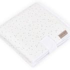 Eine gefaltete KraftKids Reisewickelunterlage Musselin mit goldenen Punkten auf Weiß und Stoffetikett am Rand liegt auf weißem Hintergrund.
