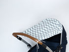 Nahaufnahme eines Kinderwagens mit einem KraftKids Sonnensegel Chevron hellgrau und mint als Sonnenschutz und einem braunen Lenker, vor einem schlichten weißen Hintergrund.