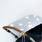 Der KraftKids Sonnensegel große weiße Sterne auf Grau ist ein hellgraues Kinderwagenverdeck mit großen weißen Sternen, hergestellt aus atmungsaktiver Baumwolle. Abgebildet auf einem Kinderwagen mit braunem Griff und dunkelmarinefarbenem Sitz vor einem schlichten weißen Hintergrund.