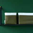 Zwei KraftKids Körbchen Doppelkrepp Grün Herbstgrün mit weißen Manschetten sitzen nebeneinander auf einem schwarzen Regal und bieten stilvolle Aufbewahrung vor einer dunkelgrünen Wand - perfekt für jeden Wickeltisch.