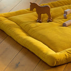 Die KraftKids Krabbeldecke Doppelkrepp Gelb Senf, eine weiche gelbe Steppmatte, liegt zusammen mit einem Spielzeugpferd und Bauklötzen auf einem Holzboden, der in warmes Sonnenlicht getaucht ist und eine gemütliche Spielszene bietet.