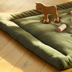 Die KraftKids Krabbeldecke Doppelkrepp Grün Herbstgrün aus weichem Polyestervlies liegt auf einem Holzboden mit Spielklötzen und einem kleinen Pferd darauf, beleuchtet vom natürlichen Sonnenlicht.