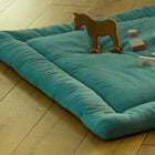 Die gepolsterte KraftKids Krabbeldecke Doppelkrepp Grün Jade liegt auf einem Holzboden mit Holzspielzeug wie einem Pferd und verschiedenen Bauklötzen. Die Matte hat eine weiche Polyestervliesfüllung für zusätzlichen Komfort.