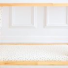 Ein KraftKids Spannbettlaken Musselin Zweige braun bedeckt die Matratze auf einem hölzernen Bettrahmen mit gemusterten weißen Vorhängen, die vor einer weißen Wand mit Zierleisten stehen.